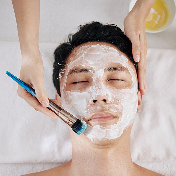 Beautifcian using brush when applying moisturizing mask on face of Asian customer, view from above